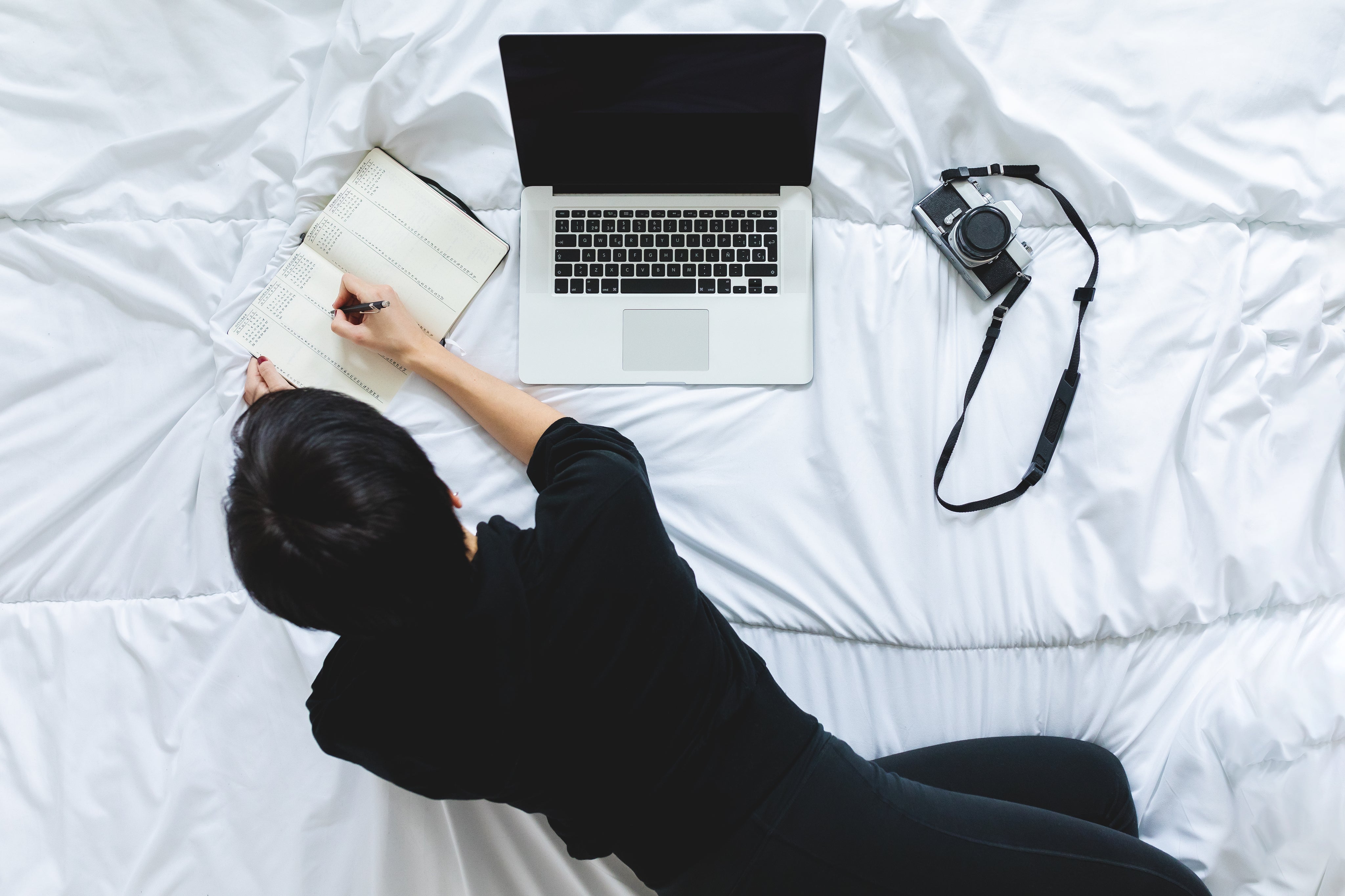 person-writing-in-notebook-beside-laptop-working-from-bed.jpg